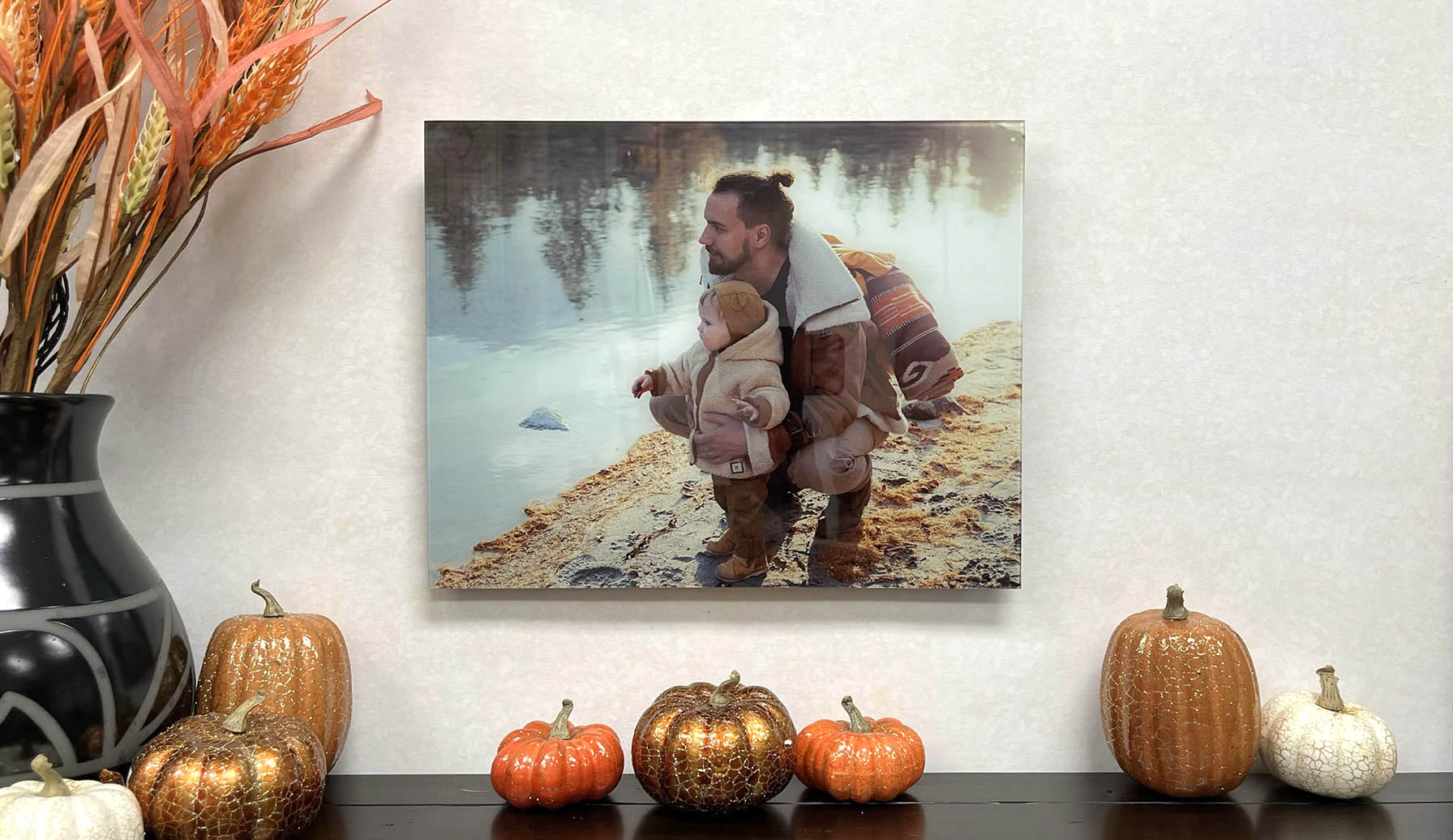 A custom print is shown displayed on the wall and surrounded by fall decor. The custom print depicts a father and son by the lake.